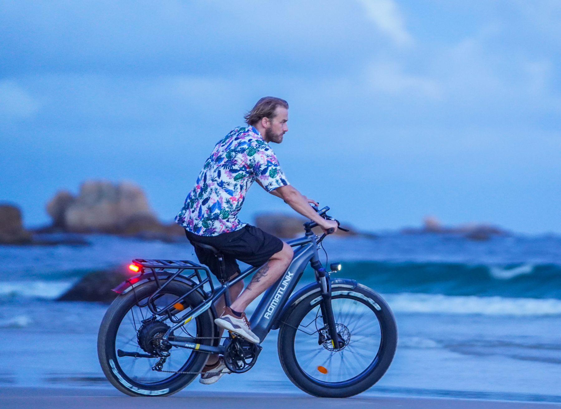 An adult man riding a Romatlink Rhino 750W, 20Ah, 48V Electric bike along the beach